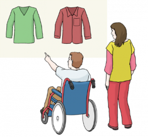 Das Bild zeigt einen Mann im Rollstuhl. Eine Freu steht neben ihm. Vor dem Mann hängen zwei Kleidungsstücke. Der Mann zeigt mit dem Finger aus eins von beiden.