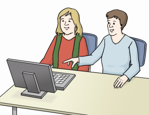 Das Bild zeigt zwei Personen, die vor einem Computer sitzen. Eine Person zeigt etwas im Computer.